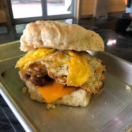 A biscuit sandwich filled with cheese, sausage, and a fried egg, served on a metal tray.