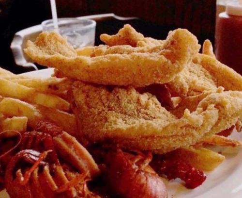 A plate of fried fish fillets with crispy fries and a side of crawfish.