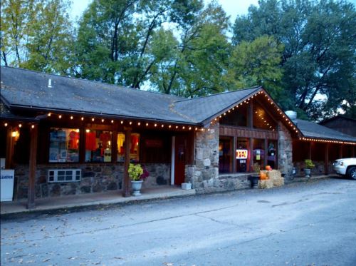 A rustic building with stone and wood exterior, adorned with string lights, surrounded by trees and autumn decorations.