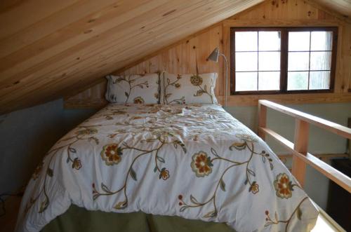 Cozy attic bedroom with a sloped wooden ceiling, featuring a floral-patterned bedspread and two windows.