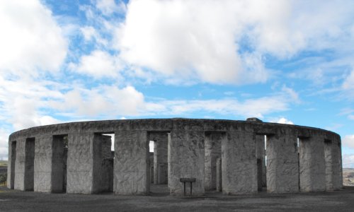 A stone circle structure under a blue sky with clouds, resembling ancient architecture.