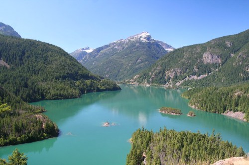 A serene lake surrounded by lush green forests and mountains under a clear blue sky.