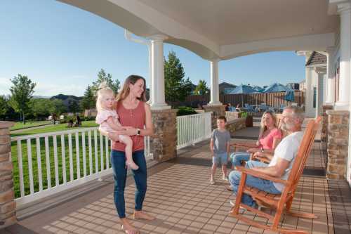 A family enjoys time together on a porch, with a woman holding a child and two adults sitting in rocking chairs.