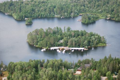 Aerial view of a lush green island surrounded by a winding lake, with boats docked along a wooden pier.