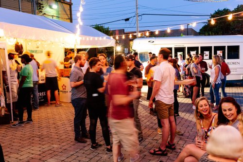 A lively outdoor event with people socializing, a tent, and string lights in the evening.