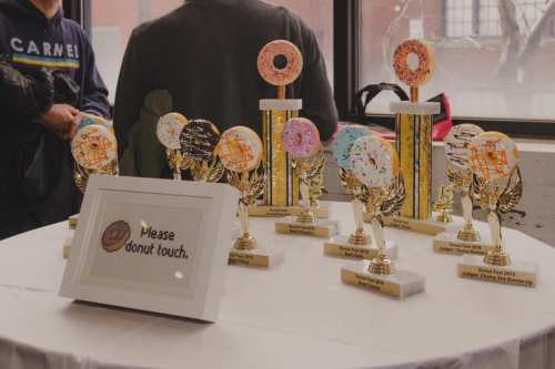 Trophies with donut designs on a table, alongside a sign that says "Please donut touch." Window in the background.