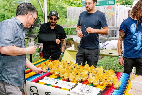 A group of men examines colorful dishes at a food event, with vibrant tablecloths and a festive atmosphere.