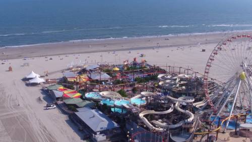 Aerial view of a beach amusement park with rides, water slides, and a Ferris wheel by the ocean.