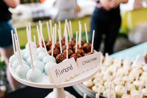 A display of colorful cake pops on a stand, labeled "Almond" and "Chocolate," with a variety of sprinkles.