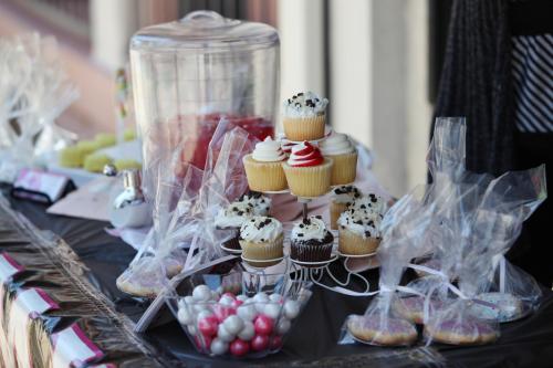 A display of colorful cupcakes on a stand, surrounded by candy and treats in clear bags on a decorated table.