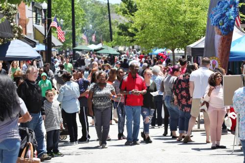 A busy street filled with people browsing tents at an outdoor market on a sunny day.