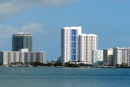 City skyline featuring modern high-rise buildings along a waterfront under a clear blue sky.
