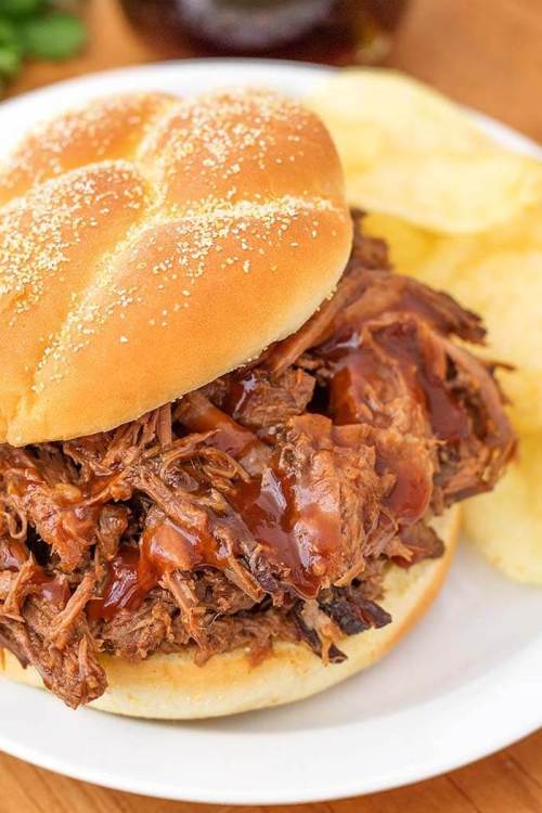 A pulled pork sandwich with barbecue sauce on a soft bun, served with potato chips on the side.