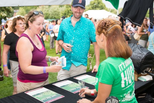 A group of people at an outdoor event, interacting at a table with informational materials and drinks in hand.