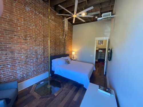 Cozy bedroom with exposed brick walls, a ceiling fan, a bed, and a unique glass floor feature.