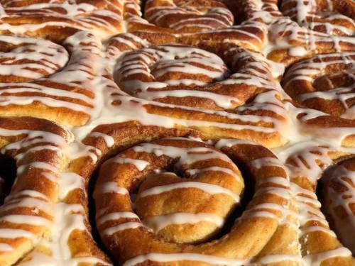 Close-up of freshly baked cinnamon rolls drizzled with white icing, showcasing their swirled texture.