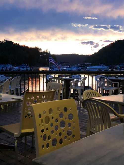 Sunset over a lake with boats, featuring outdoor seating and an American flag in the background.