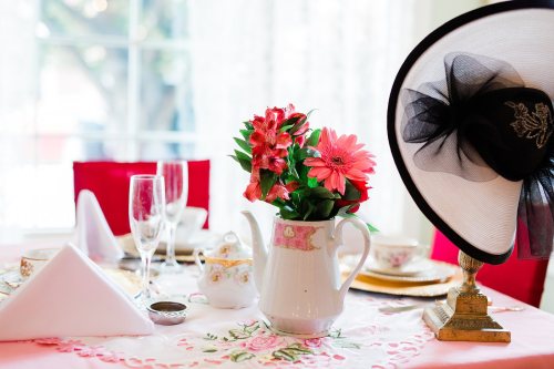 A table set for tea with a floral centerpiece, elegant teacups, and a decorative hat on display.