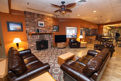 Cozy lounge area with leather sofas, a fireplace, and a patterned rug, featuring warm lighting and a welcoming atmosphere.