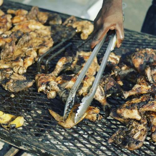 A hand using tongs to flip grilled chicken on a barbecue grill, with various pieces of meat sizzling.