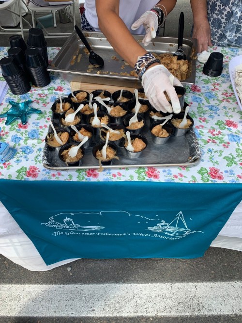 A table with a floral tablecloth displaying small cups of food being served by a person wearing gloves.