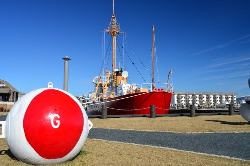 A red ship docked near a large white buoy marked with a "G," set against a clear blue sky.