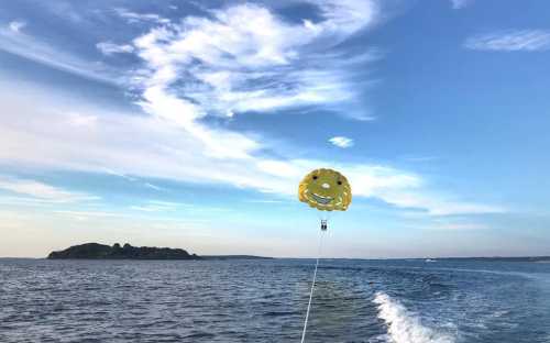 A person parasailing with a yellow smiley face parachute over a calm blue sea, with an island in the background.