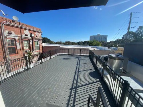 A spacious rooftop deck with a railing, overlooking buildings and a clear blue sky.