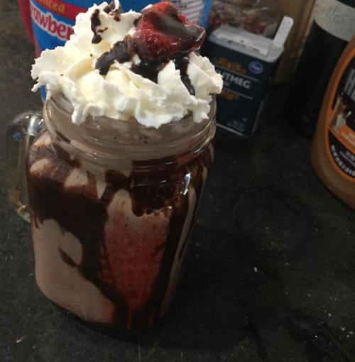 A mason jar filled with chocolate milkshake, topped with whipped cream, chocolate syrup, and a strawberry.