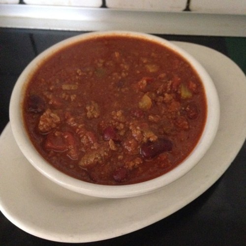 A bowl of hearty chili with beans and ground meat, served on a white plate against a dark background.