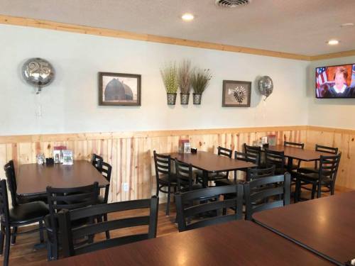 Interior of a restaurant with wooden walls, tables, and chairs, featuring decor and a TV on the wall.