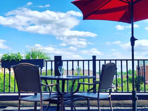 A sunny outdoor patio with a red umbrella, two empty glasses, and a view of greenery and blue skies.