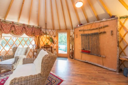 Cozy interior of a yurt with wicker chairs, wooden decor, and a door leading outside. Warm, inviting atmosphere.