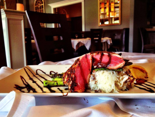 A beautifully plated dish featuring grilled salmon, asparagus, and rice drizzled with sauce, set in an elegant restaurant.