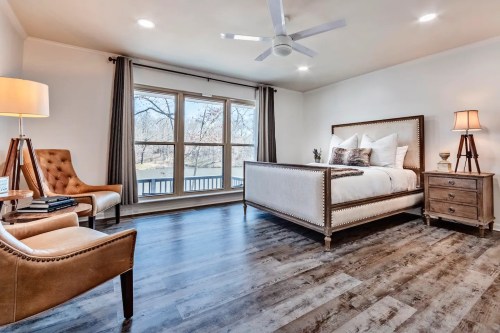A modern bedroom featuring a bed, armchair, nightstand, and large windows with natural light.