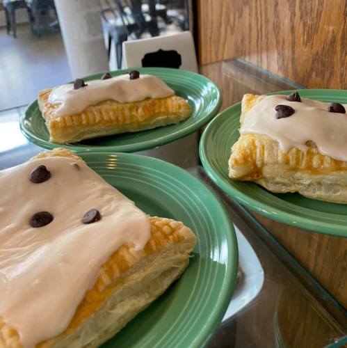 Three pastries on green plates, topped with pink icing and chocolate chips.