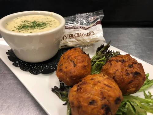 A plate with three golden-brown fritters on greens, accompanied by a bowl of creamy soup and oyster crackers.