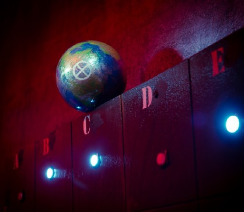 A colorful globe rests on a dark surface with labeled sections and glowing lights, set against a red background.