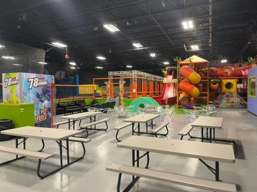 Indoor play area with colorful slides, climbing structures, and tables for seating. Brightly lit and spacious.