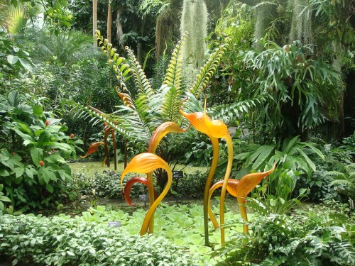Vibrant orange glass sculptures resembling flowers amidst lush greenery in a tropical garden.