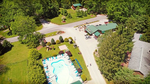 Aerial view of a resort with a pool, surrounded by greenery and a road, featuring cabins and landscaped areas.