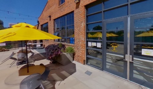 Outdoor seating area with yellow umbrellas, brick building, and large windows.