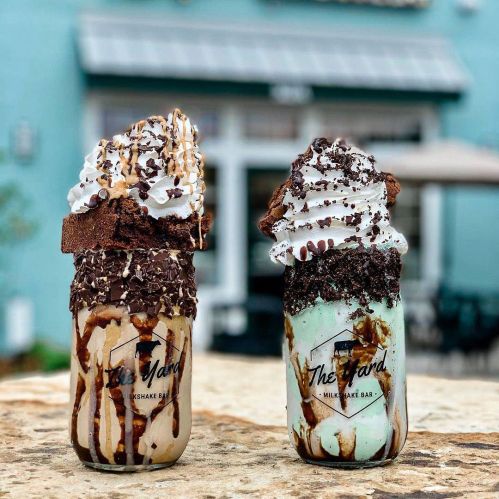 Two decadent milkshakes topped with whipped cream, chocolate, and brownie, served in mason jars from The Yard Milkshake Bar.