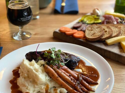 A plate of mashed potatoes, glazed carrots, and beef with sauce, alongside a charcuterie board and a dark beer.