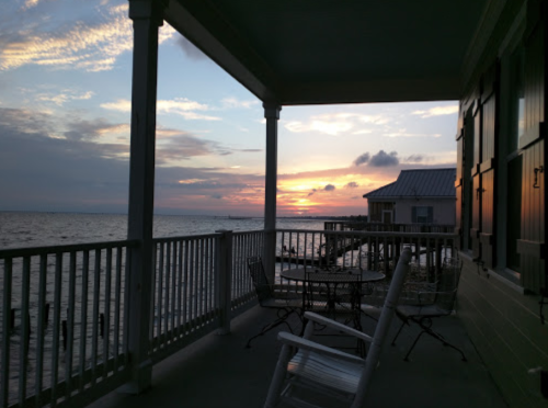 Sunset view from a porch overlooking the water, with chairs and a table in the foreground.