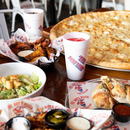 A table spread with a large pizza, wings, salad, drinks, and dipping sauces at a casual dining restaurant.
