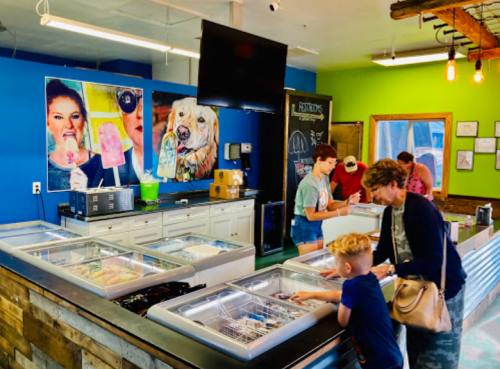 A colorful ice cream shop with customers at the counter and vibrant artwork on the walls.