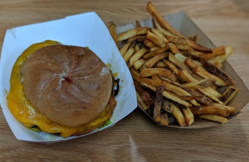A cheeseburger with melted cheese on a bun, served with a side of crispy French fries in a paper container.