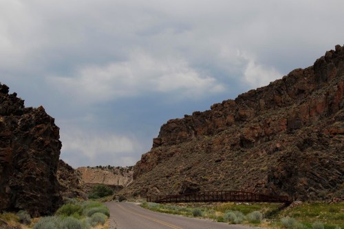 A winding road between rocky cliffs under a cloudy sky, with sparse vegetation along the sides.