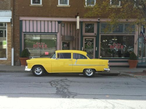 A bright yellow vintage car parked in front of a diner with large windows and a classic sign.